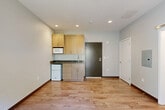 Located at 4025 Rainier Ave S in Seattle's Rainier Beach neighborhood, this studio apartment offers a thoughtfully designed, single-floor layout that maximizes every square foot. The open-concept living area features warm hardwood-style flooring throughout, neutral gray walls, and recessed lighting that keeps the space feeling bright and modern. A compact kitchenette is efficiently outfitted with light wood cabinetry, dark countertops, a stainless steel sink, a built-in microwave, and a mini refrigerator — providing all essential cooking conveniences in a space-conscious footprint. The living and dining area is anchored by a sliding glass door that fills the room with natural light and opens directly onto a private patio. The patio is enclosed by a horizontal-slat privacy fence and features a raised concrete planter bed with established greenery, creating a pleasant outdoor retreat. A sliding barn-style door leads to a closet, adding a stylish, space-saving touch. The bathroom and an additional room complete the layout. A wall-mounted mini-split unit provides climate control, and the clean, contemporary finishes throughout give the unit a cohesive, move-in-ready aesthetic ideal for urban living.