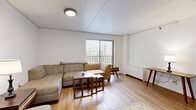 Located in State College, PA, this two-bedroom, one-bathroom unit is laid out across a single floor, offering a straightforward and functional arrangement of living spaces. The living room serves as the central gathering area, featuring light hardwood-style flooring, white walls, and a large window fitted with vertical blinds that brings in natural light and outdoor views of the surrounding neighborhood. The kitchen is a compact, efficient space highlighted by warm cherry-toned cabinetry, granite-style countertops, tile flooring, and a bold accent wall, with standard appliances including a range and refrigerator. Both bedrooms are carpeted in a deep blue tone and maintain a clean, simple aesthetic with white walls. The spacious primary bedroom includes a window with outdoor views and ample room for furnishings, while the second bedroom also features a window and a built-in closet with wood-paneled sliding doors. Three closets throughout the unit provide generous storage. The full bathroom offers a tub-shower combination with sliding glass doors, a vanity with dark wood cabinetry, and classic white mosaic tile flooring. A connecting hallway ties all rooms together for easy navigation throughout the unit.