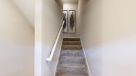 This three-story residence in Novi, Michigan offers a thoughtfully organized layout distributed across multiple levels, connected by carpeted staircases with clean white railings. The entry level provides a compact but functional introduction to the home, leading up to the main living floor, which serves as the heart of the space.

The main level hosts a spacious living room featuring striking vaulted ceilings and abundant natural light from large windows dressed with drape panels. The kitchen is outfitted with white shaker cabinetry, subway tile backsplash, stainless steel appliances, and wood-look flooring, with a sliding glass door opening onto a private balcony with neighborhood views. A dining nook adjacent to the balcony access adds casual versatility.

The upper level houses both bedrooms and two full bathrooms. The generously sized primary bedroom features mirrored sliding closet doors and soft carpet flooring. The second bedroom also includes a closet and carpeted floors. The primary bathroom offers an elongated vanity with white cabinetry and a tiled tub-shower combination, while the second bathroom mirrors this clean, neutral aesthetic with wood-look tile flooring and open shelving.
