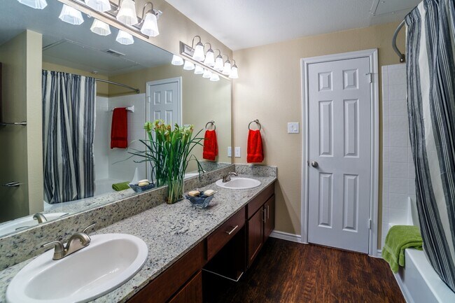 Baño con gabinetes de castaño, encimeras de granito moteado y pisos de superficie dura. - eaves North Dallas