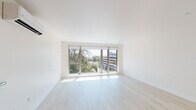 Located on the sixth floor at 1431 Q St in Sacramento's vibrant Midtown neighborhood, this contemporary apartment offers a thoughtfully designed single-floor layout with a clean, minimalist aesthetic throughout. The living area is bathed in natural light, courtesy of expansive floor-to-ceiling windows that frame treetop and city views, creating an airy and open atmosphere. Light-toned hardwood flooring runs continuously through the main living spaces, reinforcing the bright, modern feel. The kitchen is a standout feature, equipped with high-end stainless steel appliances including a professional-grade gas range and French door refrigerator. Flat-panel wood cabinetry in a warm taupe finish extends to the ceiling for ample storage, while a striking white marble-veined quartz backsplash and countertops add a refined, upscale touch. A dishwasher is also integrated seamlessly into the cabinetry. The bathroom maintains the same contemporary design language, featuring large-format tile flooring, marble-style wall tile in the shower surround, a wood-toned vanity with an undermount sink, and a sleek illuminated mirror. Recessed lighting throughout ensures consistent, well-distributed illumination across all areas. The overall design is cohesive and sophisticated, emphasizing clean lines, premium materials, and a neutral palette.