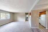 Located at 900 Post Rd in Warwick, Rhode Island, this two-bedroom, one-bathroom unit offers a practical and comfortable single-floor layout. The combined kitchen and living area serves as the heart of the home, where the kitchen features warm wood cabinetry, granite-look countertops, light wood-style vinyl flooring, and white appliances including a gas range and refrigerator. The living area extends from the kitchen and is brightened by a large multi-pane window offering views of surrounding greenery, with a wall-mounted A/C unit and baseboard heating ensuring year-round comfort. A ceiling fan adds to the functionality of this shared space. Both bedrooms are carpeted in neutral tones with soft gray walls, creating a calm and restful atmosphere. The primary bedroom is generously sized and includes a dedicated closet, while the second bedroom also benefits from natural light through its own window and access to a walk-in closet. A hallway connects the bedrooms and leads to the full bathroom, which is equipped with a tub and shower combination. Baseboard heating is present throughout the unit, and the textured ceilings add a classic residential character to the overall space.