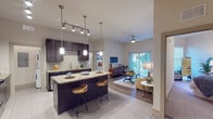 This single-floor residence at 5290 Big Island Drive in Jacksonville, Florida, presents a thoughtfully designed open-concept layout that seamlessly connects the kitchen, dining, and living areas. The kitchen is a standout feature, outfitted with rich dark espresso cabinetry extending to the ceiling, granite countertops, a tile backsplash, and stainless steel appliances including an electric range and built-in microwave. A central island with bar seating serves as both a functional workspace and a casual dining area, illuminated by modern pendant lighting. Track lighting overhead adds further versatility to the space.

The living area transitions naturally from the kitchen, featuring wood-look flooring, a ceiling fan, and large sliding glass doors that open to a private balcony, allowing abundant natural light. The space accommodates comfortable seating and a media area with ease.

Two bedrooms feature plush carpeting, natural light from windows, and generous walk-in closets outfitted with wire shelving systems. The primary bathroom includes dark vanity cabinetry with granite counters, a large mirror, tile flooring, and a tub-shower combination. An in-unit laundry area with a washer and dryer completes this well-appointed residence.
