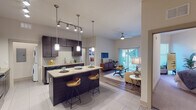 This single-floor residence at 5290 Big Island Drive in Jacksonville, Florida, presents a thoughtfully designed open-concept layout that seamlessly connects the kitchen, dining, and living areas. The kitchen is a standout feature, outfitted with rich dark espresso cabinetry extending to the ceiling, granite countertops, a tile backsplash, and stainless steel appliances including an electric range and built-in microwave. A central island with bar seating serves as both a functional workspace and a casual dining area, illuminated by modern pendant lighting. Track lighting overhead adds further versatility to the space.

The living area transitions naturally from the kitchen, featuring wood-look flooring, a ceiling fan, and large sliding glass doors that open to a private balcony, allowing abundant natural light. The space accommodates comfortable seating and a media area with ease.

Two bedrooms feature plush carpeting, natural light from windows, and generous walk-in closets outfitted with wire shelving systems. The primary bathroom includes dark vanity cabinetry with granite counters, a large mirror, tile flooring, and a tub-shower combination. An in-unit laundry area with a washer and dryer completes this well-appointed residence.
