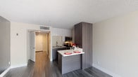 Located at 606 3rd Ave, Unit B12 in San Diego, this single-floor residence features a thoughtfully designed open layout with modern finishes throughout. The kitchen is a standout feature, offering a galley-style configuration with dark wood-grain lower cabinetry, crisp white upper cabinets, and stainless steel appliances including a refrigerator, range, and microwave. A peninsula with a white countertop provides additional prep space and a casual dining area. Wood-style plank flooring in a cool gray tone extends throughout the unit, lending a cohesive and contemporary feel. The open living area is bathed in natural light from a large floor-to-ceiling window with vertical blinds, creating a bright and airy atmosphere. A bold dark accent wall adds depth and contrast to the living space. The bathroom maintains the same clean aesthetic with white walls, dark wood-grain cabinetry, and matching flooring, complemented by recessed lighting. The textured ceiling and neutral wall tones throughout the unit contribute to a modern yet understated design. Overall, the space offers a well-appointed, efficiently designed interior suited for contemporary urban living in the heart of San Diego.
