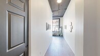 Located in the heart of downtown Spokane at 107 S Howard Street, Unit 204 is a thoughtfully designed studio that makes efficient use of its single-floor layout. The space is entered through a clean, well-lit hallway featuring light hardwood flooring, crisp white walls, exposed ceiling ductwork with an industrial aesthetic, and understated wall sconces that set a modern tone throughout.

The open-plan living area is a standout feature, defined by a dramatic bank of large, black-framed windows that flood the room with natural light and offer direct views of the surrounding urban streetscape. The dark ceiling treatment contrasts boldly with the bright walls, lending the living space a loft-like character. Hardwood-style flooring continues throughout, grounding the open layout.

The kitchen is well-appointed with natural wood cabinetry, a classic white subway tile backsplash, stainless steel appliances including a refrigerator, dishwasher, and range, and ample counter space. A dedicated dining area sits adjacent to the kitchen, complemented by a wall-mounted display and a window with city views, creating a functional yet inviting everyday living space.

Overall, Unit 204 combines industrial-inspired architectural details with warm, modern finishes in a prime downtown Spokane location.
