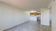 Located in Avondale, Arizona, this single-story 2-bedroom, 2-bathroom home offers a functional and straightforward layout designed for comfortable everyday living. The open-concept living and dining area is finished with light wood-tone luxury vinyl plank flooring and neutral white walls, creating a bright, clean atmosphere. A large window with vertical blinds allows natural light to fill the living room, which also features a front entry door and a textured ceiling throughout.

The kitchen is positioned adjacent to the living area and is defined by a peninsula-style breakfast bar with a white countertop. Warm wood-toned cabinetry lines the kitchen walls, complemented by a white electric range and refrigerator. A set of open built-in shelves beside the kitchen adds convenient storage and display space.

Both bedrooms are carpeted and offer a quiet, comfortable retreat. The primary bedroom includes a spacious walk-in closet, while the second bedroom features a sliding double-door closet. Each bedroom is served by its own bathroom — one featuring wood-toned vanity cabinetry, a white countertop, and an adjacent walk-in closet area. The cinder block wall construction visible in the primary bedroom speaks to the home's solid, durable build. Textured ceilings are consistent throughout the residence.