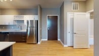 This single-floor unit offers a thoughtfully designed layout with a cohesive, modern aesthetic throughout. The kitchen is a functional standout, featuring two-tone cabinetry with dark lower cabinets and crisp white upper cabinets, light quartz countertops, stainless steel appliances including a refrigerator, range, microwave, and dishwasher, a stainless steel sink, and a built-in wine rack. Light wood-look flooring runs through the kitchen and entry areas, adding warmth and continuity.

The entry area provides a clean transition into the living spaces, with a wood-toned front door, a utility closet, and open sightlines to the kitchen. The bedrooms are carpeted and painted in neutral gray-taupe tones, each equipped with a ceiling fan and windows that bring in natural light. One bedroom includes additional access to an adjoining space, offering flexible use.

Both bathrooms share a consistent design language, featuring wood-grain tile flooring, dark walnut-toned vanity cabinetry with white countertops, a full tub-shower combination with a curved curtain rod, and chrome hardware accents. The warm taupe wall color ties the bathrooms together with the rest of the unit. Overall, the space presents a clean, contemporary feel with practical finishes suited for everyday living.