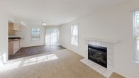 This single-floor residence offers a thoughtfully designed layout that balances comfort and functionality throughout its connected living spaces. The living area is a bright, welcoming room anchored by a tile-surround fireplace with a clean white mantle, complemented by plush carpeting and multiple windows dressed with vertical blinds that allow generous natural light to filter in. Adjacent hardwood-style flooring transitions the space toward the kitchen area, adding visual contrast and warmth.

The kitchen is a standout feature, equipped with light wood cabinetry, dark stone-toned countertops, and a peninsula with a built-in cooktop — ideal for both meal preparation and casual dining. White appliances, including a refrigerator, electric range, and dishwasher, are neatly integrated, while recessed lighting overhead enhances the functional atmosphere. A window above the sink brings in additional natural light.

The bedrooms are carpeted and offer a calm, neutral palette, each featuring sliding mirrored closet doors. One bedroom includes a spacious walk-in closet with dual wooden hanging rods, providing generous storage capacity. The bathroom is finished with light wood-toned flooring, a single-sink vanity with stone-look countertops, and a full tub-shower combination enclosed by sliding glass doors.