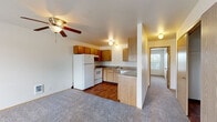 This single-floor unit offers a practical and functional layout centered around an open-concept living and kitchen area. The kitchen is equipped with warm oak cabinetry — both upper and lower — complemented by laminate countertops, a double stainless steel sink, a dishwasher, a white refrigerator, and an electric range. A partial wall with a built-in breakfast bar separates the kitchen from the living area, creating a semi-open feel while maintaining defined spaces. The kitchen features hardwood-style flooring, while the living area is finished with neutral wall-to-wall carpeting and includes a ceiling fan with a light fixture overhead.

A sliding glass door in the living area opens to a private balcony, allowing natural light to filter in alongside views of the surrounding neighborhood greenery. Additional windows with blinds are present throughout, including in the carpeted bedrooms, which are well-sized and feature flush-mount lighting. The bathroom includes a single-sink vanity with a wood cabinet base, a laminate countertop, a wall-mounted mirror, and a full tub and shower combination with a curtain rod. Luxury vinyl plank flooring completes the bathroom. Overall, the unit presents a clean, straightforward design with consistent finishes throughout.