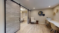 Located in Somerset, NJ, this thoughtfully designed single-floor professional office space blends contemporary style with functional efficiency. Light-toned luxury vinyl plank flooring runs throughout, creating a cohesive and clean aesthetic across all areas.

The reception area sets a welcoming tone, featuring a plush white accent chair, a decorative wood side table, and an artistic wall arrangement of overlapping metallic and navy disc sculptures. Adjacent to this seating area is a compact workstation equipped with a printer, ideal for administrative tasks.

A striking pair of sliding barn doors with weathered wood panels and black metal hardware serve as a dramatic and practical divider between the reception space and the main conference or meeting room. The meeting room is anchored by a rectangular table surrounded by sleek white rolling chairs, illuminated by a stylish geometric pendant light fixture. A wall-mounted mini-split HVAC unit ensures year-round comfort, and a window allows natural light and views of the surrounding neighborhood.

A separate consultation room offers an intimate setting with two soft cream armchairs flanking a marble-top gold side table, accented by an abstract canvas artwork overhead — ideal for private client meetings.

Recessed lighting throughout provides consistent, even illumination, while the neutral warm-beige walls and curated décor contribute to a calm, professional ambiance.