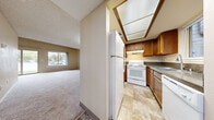 Located at 2455 George Washington Way in Richland, WA, this two-story home offers four bedrooms and four bathrooms across a well-organized floor plan. The main level houses the entrance, a combined kitchen and living room, an additional living room, and two closets, while the upper level accommodates the remaining bedrooms and bathrooms.

The kitchen is equipped with warm oak cabinetry, dark countertops, white appliances including a range, refrigerator, and dishwasher, and features a distinctive skylight overhead that fills the space with natural light. Stone-look tile flooring flows throughout the kitchen and bathrooms, providing a clean, durable surface.

The living areas are carpeted in neutral tones and benefit from natural light through large windows. Notable architectural details include vaulted ceilings on the upper floor, lending an open, airy feel to the bedrooms. The generously sized primary bedroom features a vaulted ceiling and a window with outdoor views of surrounding greenery.

Each bathroom is finished with matching stone-look tile flooring and oak vanities with granite-style countertops. A staircase connects the two floors, and the overall color palette of warm beige and cream tones creates a cohesive, understated ambiance throughout the home.