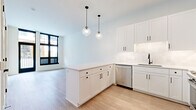 This well-appointed 2-bedroom, 2-bathroom residence offers a thoughtfully designed single-floor layout that maximizes functionality and style. The interior is finished in a clean, modern aesthetic throughout, with crisp white walls and light wood-look flooring in the main living areas transitioning to plush carpet in the bedrooms.

The kitchen is a standout feature, showcasing white shaker cabinetry with gold hardware, quartz countertops, a glossy white tile backsplash, and a full suite of stainless steel appliances including a gas range with a stainless hood vent. A gold-finish faucet adds an elegant touch, while a large black-framed window provides ample natural light and an outdoor view.

The living area is generously proportioned, with light flooring and open sightlines that contribute to an airy atmosphere. The primary bedroom offers a comfortable footprint with oversized black-framed windows on two walls, inviting abundant natural light and exterior views. The second bedroom features soft carpeting and well-proportioned walls.

Both bathrooms are finished with modern cabinetry and wood-look flooring. One bathroom features a walk-in glass-enclosed shower with large-format marble-look tile and matte black fixtures. The hallway connects all rooms efficiently, and two closets provide practical storage throughout the residence.