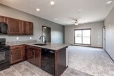 Located at 2861 Prairie Hill Dr in Marion, Iowa, this well-appointed 2-bedroom, 2-bathroom single-floor home offers a thoughtfully designed open-concept layout. The combined kitchen, dining, and living area serves as the heart of the home, featuring rich dark wood cabinetry, granite countertops with an undermount sink, a peninsula island, and black appliances including a refrigerator, range, and microwave. Large tile flooring runs throughout the kitchen, transitioning to plush carpet in the living area, which is brightened by a broad window and a ceiling fan overhead. A door from the living space leads directly to an outdoor balcony, providing pleasant exterior views. The primary bedroom is a comfortable retreat with carpeted floors, a ceiling fan, a large window, and generous closet space with wire shelving. The second bedroom is equally well-sized with carpet and natural light. Both bathrooms are finished with tile flooring and dark wood vanities topped with framed mirrors. A dedicated laundry room with tile flooring adds everyday convenience. A hallway connects all areas cohesively, with dark wood-trimmed doors and warm neutral tones throughout creating a clean, modern ambiance.
