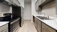 This single-floor residential unit offers a thoughtfully designed layout with a clean, contemporary aesthetic throughout. The galley-style kitchen is a standout feature, showcasing gray shaker cabinetry with brushed nickel hardware, light marble-look countertops, a stainless steel sink, and a tasteful subway tile backsplash. Stainless steel appliances, including a refrigerator and range, complete the functional cooking space. Light wood-look flooring runs through the kitchen, adding warmth and easy maintenance underfoot.

The living area is spacious and carpeted, bathed in natural light through a sliding glass door that opens to a private balcony enclosed with vertical blinds. A front entry door provides direct access to this open, welcoming common area. The bedrooms are generously sized, each carpeted and finished with neutral-toned walls, offering a calm and comfortable atmosphere. Windows with blinds allow natural light into the sleeping areas while maintaining privacy.

The bathroom is well-finished, featuring a full tub-and-shower combination with white subway tile surround, wood-look flooring, and gray cabinetry with a light countertop at the vanity. Throughout the unit, consistent neutral tones, clean white baseboards, and modern finishes create a cohesive, move-in-ready environment.