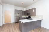 Located at 118 E Sego Lily Dr in Sandy, UT, this thoughtfully designed one-bedroom, one-bathroom unit offers a cohesive modern aesthetic throughout its single floor. The open-concept kitchen and living area serves as the heart of the home, featuring rich wood-style flooring, contemporary dark-grain cabinetry, a white quartz peninsula with an undermount sink, and stylish pendant lighting. Stainless steel appliances — including a refrigerator, gas range, and microwave — complement the subway tile backsplash for a clean, polished look. The living area flows naturally toward a sliding glass door dressed with vertical blinds, allowing abundant natural light and providing access to an outdoor area. The bedroom is a calm retreat with soft carpet flooring, neutral walls, and a bright window with views of the surrounding greenery. A dedicated walk-in closet offers wire shelving along multiple walls for generous storage. The bathroom is finished with a framed vanity mirror, dark cabinetry with a white countertop, and a full soaking tub with subway tile surround. A hallway connects the spaces efficiently, completing this well-appointed and move-in-ready residence.