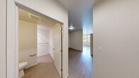 Located at 4302 7th Ave NE in Seattle's vibrant University District, this efficiently designed single-floor unit makes smart use of its compact footprint. The open layout is anchored by light hardwood-style flooring that runs throughout the main living area, creating a clean and cohesive aesthetic.

The kitchen is a functional highlight of the space, outfitted with warm wood cabinetry, white countertops, and a full suite of stainless steel appliances including a refrigerator, range, microwave, and dishwasher. Track lighting above the kitchen ensures well-lit meal preparation, while a double-pane window alongside the kitchen area invites natural light and views of the surrounding greenery.

The hallway connects the main living zone to the bathroom and additional storage areas, finished with neutral carpet and clean white walls for a bright, open feel. The bathroom features a wood-toned vanity with an integrated sink and access to a separate carpeted closet or utility area. A HVAC vent system ensures year-round climate comfort throughout the unit.

The main living area offers a versatile, open canvas with hardwood-style flooring, white walls, and natural light filtering in from nearby windows. This well-organized unit provides a practical and comfortable living environment in one of Seattle's most walkable and transit-accessible neighborhoods.