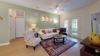 This single-floor residence offers a thoughtfully designed layout that balances functionality and comfort throughout its key living spaces. The living room serves as a central gathering area, featuring warm hardwood-style flooring, a ceiling fan, and a sage green accent wall that lends a calm, inviting atmosphere. French doors provide natural light and outdoor views, while decorative wall art adds character to the space.

Adjacent to the living room, the dining area continues the hardwood-style flooring and is anchored by a chandelier overhead. The sage green accent wall carries through cohesively from the living space, creating a unified aesthetic.

The kitchen is well-equipped with warm wood cabinetry, granite-look countertops, black appliances including a refrigerator and range, and a center island with a built-in sink. The layout offers generous counter and storage space, with a laundry area accessible nearby.

Both bedrooms feature plush carpeting, ceiling fans, and ornamental wall décor. One bedroom benefits from a natural light-filled window with views of surrounding greenery. Each bathroom includes a wood-toned vanity with ample cabinet storage, lighted mirror, and tile flooring, providing practical and clean finishing details throughout.