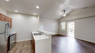 Located at 827 E Riverside Dr, Unit 224 in Eagle, Idaho, this single-floor residence features a clean, contemporary design throughout. The kitchen is well-appointed with warm walnut-toned cabinetry, white quartz countertops, stainless steel appliances including a refrigerator, electric range, built-in microwave, and dishwasher, all set atop light wood-look flooring. A peninsula with a double stainless steel sink extends into the adjoining living area, which features vaulted ceilings, recessed lighting, a ceiling fan, and sliding glass doors that open to a private balcony, allowing natural light to fill the space. The bedrooms are carpeted and offer windows with views of the surrounding neighborhood. Two full bathrooms are finished with warm wood vanities, white quartz countertops, and distinctive hexagonal tile flooring, each providing a tub-shower combination and brushed nickel fixtures. A dedicated laundry area is equipped with a stacked washer and dryer unit, conveniently accessible from the main living space. The overall aesthetic is modern and neutral, with white walls, clean lines, and consistent finishes creating a cohesive and move-in ready environment throughout.