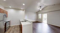 Located at 827 E Riverside Dr, Unit 224 in Eagle, Idaho, this single-floor residence features a clean, contemporary design throughout. The kitchen is well-appointed with warm walnut-toned cabinetry, white quartz countertops, stainless steel appliances including a refrigerator, electric range, built-in microwave, and dishwasher, all set atop light wood-look flooring. A peninsula with a double stainless steel sink extends into the adjoining living area, which features vaulted ceilings, recessed lighting, a ceiling fan, and sliding glass doors that open to a private balcony, allowing natural light to fill the space. The bedrooms are carpeted and offer windows with views of the surrounding neighborhood. Two full bathrooms are finished with warm wood vanities, white quartz countertops, and distinctive hexagonal tile flooring, each providing a tub-shower combination and brushed nickel fixtures. A dedicated laundry area is equipped with a stacked washer and dryer unit, conveniently accessible from the main living space. The overall aesthetic is modern and neutral, with white walls, clean lines, and consistent finishes creating a cohesive and move-in ready environment throughout.