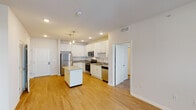 This well-appointed single-floor residence offers a thoughtfully designed layout that balances functionality and modern style. The heart of the home is an open-concept kitchen, which features crisp white shaker cabinetry, granite-look countertops, and a full suite of stainless steel appliances including a refrigerator, electric range, over-the-range microwave, and dishwasher. A central kitchen island provides additional prep space and a natural gathering point. Pendant lighting overhead adds a warm, contemporary touch, while recessed lighting ensures the space is well-lit throughout. Light hardwood-style flooring extends through the kitchen and living areas, contributing to a clean, cohesive aesthetic. The living room is bright and open, with large windows fitted with blinds that allow for ample natural light and outdoor views. The bedrooms are carpeted for comfort and also feature windows that bring in natural light. The primary bathroom is finished with granite-topped vanity cabinetry and direct access to a walk-in closet with wire shelving. A dedicated laundry closet houses a front-loading washer, adding everyday convenience. Overall, the space presents a clean, modern palette with neutral tones throughout.