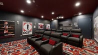 Located at 750 Summer St in Stamford, CT, this purpose-built private screening room is a meticulously themed cinematic retreat inspired by the iconic James Bond franchise. The space is anchored by a large projection screen at one end of the room, paired with a ceiling-mounted projector that delivers an immersive viewing experience. Two tiered rows of plush, dark leather reclining seats — each equipped with built-in cup holders and accented with bold red throw pillows — provide comfortable, unobstructed sightlines to the screen. The deep charcoal-textured walls and rich burgundy ceiling create an intimate, theater-like ambiance, while recessed lighting sets the mood throughout. The floors are covered in a striking Union Jack-patterned carpet that reinforces the British spy aesthetic. Classic James Bond movie posters, including iconic titles such as Dr. No, Goldfinger, and The Man with the Golden Gun, adorn the walls, adding an authentic collector's touch. A compact kitchenette area along one wall includes cabinetry, a microwave, and a popcorn machine, ensuring guests are fully equipped for the ultimate movie night. The room offers a self-contained, highly curated entertainment experience from every seat.