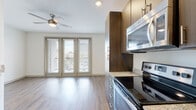 This well-appointed single-floor unit offers a thoughtfully designed layout that balances functionality and modern aesthetics throughout. The open-concept living and kitchen area is anchored by large French-style doors that flood the space with natural light and provide access to an outdoor balcony, complemented by a ceiling fan that enhances airflow and comfort.

The kitchen is a standout feature, equipped with a full suite of stainless steel appliances including a range with oven, over-the-range microwave, refrigerator, and dishwasher. Rich, dark wood cabinetry with sleek bar-pull hardware extends floor to ceiling, providing generous storage, while granite countertops add a refined, durable work surface. The galley-style layout promotes efficient workflow and connects seamlessly to the open living area.

Warm wood-look plank flooring runs continuously through the living spaces and bedrooms, lending a cohesive, contemporary feel throughout. The bedrooms are bright and versatile, each featuring ceiling fans and clean white walls that offer a neutral backdrop for personalization.

The bathroom is cleanly finished with large-format tile flooring, a full soaking tub with shower, a wide vanity mirror, and light wood cabinetry. Recessed lighting and chrome fixtures complete the polished look. Overall, this space delivers a clean, modern living environment with quality finishes at every turn.