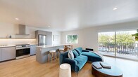 Located at 1422 Tamarind Ave in the heart of Hollywood, Los Angeles, this thoughtfully designed one-bedroom, one-bathroom unit offers a well-organized open-concept floor plan filled with natural light. Light hardwood-style flooring runs throughout the space, tying the rooms together with a warm, cohesive aesthetic.

The combined living, dining, and kitchen area forms the heart of the unit. The modern kitchen features sleek grey cabinetry, a white quartz waterfall island with bar seating, stainless steel appliances, a gas range, a subway tile backsplash, and open wooden shelving for additional storage. The dining area is set beside large windows that frame views of mature street trees, creating a bright and inviting atmosphere. The living room opens directly onto a private balcony through sliding glass doors, allowing for seamless indoor-outdoor living.

The bedroom is a calm, well-proportioned retreat with clean white walls, hardwood-style flooring, and access to two closets — one of which is a walk-in with built-in wire shelving. The bathroom is finished with floor-to-ceiling white vertical tile in the tub surround, a floating vanity with a white countertop, and a warm gold sconce fixture. The unit also includes an in-unit laundry area, adding everyday convenience to this polished Hollywood residence.
