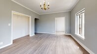 Located at 601 N Rossmore Ave in the Larchmont Village neighborhood of Los Angeles, this single-floor unit offers a well-organized layout comprising a living room, kitchen, bathroom, and two hallways. The living room is a welcoming, open space finished with light gray walls, crisp white crown molding, and smooth laminate wood flooring that runs throughout. Natural light enters through multiple windows, and an elegant gold candelabra chandelier serves as a classic centerpiece overhead. An arched alcove adds a charming architectural touch to the living area. The kitchen features white Shaker-style cabinetry with matte black hardware, granite-look countertops, and a stainless steel sink, offering a clean and functional workspace. The bathroom is a standout, showcasing floor-to-ceiling large-format blue-gray subway tiles surrounding a full soaking tub and shower combination, complemented by wood-look tile flooring for a contemporary finish. The two hallways provide efficient circulation between rooms. Consistent light-toned laminate flooring, neutral gray walls, and white trim throughout the unit create a cohesive, modern aesthetic that feels bright and well-maintained.