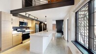 Located on Euclid Avenue in Cleveland's vibrant 44103 corridor, this two-bedroom, two-bathroom loft seamlessly blends industrial character with modern design across two floors. The main level opens with a well-appointed kitchen featuring light wood cabinetry, stainless steel appliances, a bold black tile backsplash, track lighting, and a generous white quartz island with an undermount sink — ideal for both cooking and entertaining. Polished concrete floors run throughout the main level, reflecting natural light and reinforcing the industrial aesthetic. Exposed brick walls add warmth and texture, contrasting beautifully with crisp white painted surfaces. A dramatic steel staircase with large industrial-paned windows anchors the space, flooding the interior with natural light. The upper level offers a more intimate scale, with carpeted bedrooms, exposed wood beam ceilings, and continued brick detailing. Both bathrooms are finished in a clean, contemporary style with wood vanities, white quartz countertops, black fixtures, and round backlit mirrors. A dedicated laundry area and abundant closet storage add everyday practicality to this architecturally distinctive Cleveland loft.