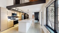 Located on Euclid Avenue in Cleveland's vibrant 44103 corridor, this two-bedroom, two-bathroom loft seamlessly blends industrial character with modern design across two floors. The main level opens with a well-appointed kitchen featuring light wood cabinetry, stainless steel appliances, a bold black tile backsplash, track lighting, and a generous white quartz island with an undermount sink — ideal for both cooking and entertaining. Polished concrete floors run throughout the main level, reflecting natural light and reinforcing the industrial aesthetic. Exposed brick walls add warmth and texture, contrasting beautifully with crisp white painted surfaces. A dramatic steel staircase with large industrial-paned windows anchors the space, flooding the interior with natural light. The upper level offers a more intimate scale, with carpeted bedrooms, exposed wood beam ceilings, and continued brick detailing. Both bathrooms are finished in a clean, contemporary style with wood vanities, white quartz countertops, black fixtures, and round backlit mirrors. A dedicated laundry area and abundant closet storage add everyday practicality to this architecturally distinctive Cleveland loft.