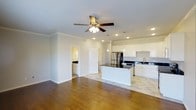 This two-story home offers a thoughtfully designed layout with modern finishes throughout. The main level showcases an open-concept living and kitchen area, where rich hardwood flooring flows seamlessly into the space, creating a warm and inviting atmosphere. Crown molding adds a refined touch to the ceilings, which are outfitted with recessed lighting and a ceiling fan, ensuring both style and comfort.

The kitchen is a standout feature, boasting crisp white cabinetry, dark granite countertops, and stainless steel appliances, including a full-size refrigerator. A central island with matching dark countertops provides additional prep space and serves as a natural gathering point. Pendant lighting hangs above the island, complementing the recessed lights throughout. A stainless steel sink is positioned beneath additional cabinetry along the perimeter, maximizing storage and functionality.

Adjacent to the main living area, a secondary space — possibly a laundry room or utility area — is visible, featuring its own countertop and lighting. A paneled interior door adds a clean, contemporary detail to the overall design. The home's neutral color palette, ample lighting, and open layout combine to create a bright, functional, and welcoming living environment across both floors.