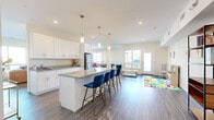 Located at 71 Connecticut Ave in Norwalk, CT, this thoughtfully designed single-floor community space offers an open-concept layout that seamlessly connects its key functional areas. The kitchen is a standout feature, showcasing crisp white shaker cabinetry, granite countertops, stainless steel appliances, and a generously sized center island with bar seating for multiple guests. Elegant pendant lighting hangs above the island, adding a polished touch to the modern aesthetic. Wide-plank wood-look flooring runs throughout, tying the entire space together cohesively. The living area is bright and welcoming, bathed in natural light from large windows that provide views of the surrounding neighborhood. Clean white walls and recessed lighting create a fresh, airy atmosphere. A wall-mounted flat-screen TV anchors the lounge zone, complemented by comfortable seating arrangements ideal for gatherings. A dedicated game room adds a recreational dimension to the space, complete with a pool table, cue rack, and additional seating—all illuminated by natural light from multiple windows. The overall ambiance is contemporary and versatile, making this space well-suited for community events, social gatherings, or everyday shared use.