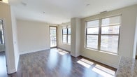This 1-bedroom, 1-bathroom residence is designed with a clean, modern aesthetic that emphasizes natural light and open living. The main living area features rich, dark hardwood-style flooring that runs throughout, creating a warm and cohesive look. Large windows with dark-framed trim line the walls, flooding the space with abundant sunlight and offering sweeping urban views of the surrounding cityscape. A glass-paneled door opens directly onto a private balcony, extending the living space outdoors and providing an ideal spot to take in the city scenery. The neutral, warm-toned walls complement the flooring and contribute to an inviting, airy atmosphere throughout. The layout is thoughtfully organized across a single floor, offering a comfortable and functional flow between spaces. White baseboards and clean architectural lines lend a polished, contemporary feel to the interior. The combination of generous window placement, outdoor access, and quality finishes makes this residence a well-appointed urban living space that balances style with practicality.