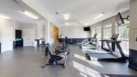 Located at 517 Yosef Dr in Boone, NC, this fitness center offers a generously sized, single-floor exercise space designed to accommodate a wide range of workout needs. The open floor plan provides ample room to move between equipment zones, with durable rubber flooring throughout that ensures both safety and comfort during exercise.

The cardio section is well-appointed with treadmills, stationary bikes, and elliptical-style machines positioned near large windows that allow natural light to fill the space. A ceiling fan overhead adds to the comfort of high-intensity workouts in this area.

The strength training section is equally comprehensive, featuring a cable and pulley multi-station machine, a power rack with barbells and weight plates, a full rack of dumbbells, and multiple selectorized resistance machines for targeted muscle training. Flat and adjustable benches are available throughout the space for added versatility.

Wall-mounted televisions are strategically placed to keep users entertained during their workouts. The interior is finished with a clean, neutral color palette — white upper walls accented by a dark lower wainscoting — giving the facility a modern and professional appearance. Fluorescent lighting ensures consistent illumination throughout the entire space, complementing the natural light from the windows. Restroom access is available within the facility.