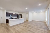 Located at 3112 Leeland St in Houston, TX, this modern single-floor residence offers a thoughtfully designed open-concept layout with clean contemporary finishes throughout. Light-toned hardwood-style flooring flows seamlessly across the entire space, complementing the crisp white walls and recessed lighting that keep the interior bright and inviting.

The heart of the home is a striking kitchen featuring dark espresso cabinetry, stainless steel appliances, and a large white waterfall-edge island with pendant lighting overhead — ideal for both cooking and casual dining. The kitchen opens directly into the living and dining areas, creating a spacious, connected feel.

The bedroom is a comfortable, well-proportioned retreat with a ceiling fan, a natural light-filled window, and access to a generously sized walk-in closet with built-in shelving and hanging rods. A dedicated office and an additional flexible room provide practical versatility for remote work or personal use.

The bathroom is finished with a sleek dark-toned vanity, white countertop, and a glass-enclosed walk-in shower with marble-style tile walls. A separate laundry area and utility room add everyday convenience.

An outdoor landing area with modern black railings, wood-deck flooring, and shiplap-clad exterior walls adds an appealing transitional space with natural light and greenery views.