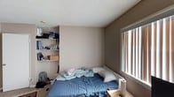 This single-floor studio is a smartly laid-out space that maximizes every square foot through an open-plan design. The main living area seamlessly integrates sleeping, dining, and workspace zones, with neutral taupe-toned walls and a textured ceiling creating a consistent, understated aesthetic throughout. Carpeted flooring covers the primary living zone, while hardwood-style flooring transitions into the kitchen area, adding a practical contrast in materials.

The kitchen is well-equipped with warm wood cabinetry, granite-look countertops, and a full suite of stainless steel appliances including a gas range with double oven and an over-the-range microwave. A black refrigerator anchors the kitchen corner, and the layout allows for easy flow into the dining and living space.

Natural light enters through windows fitted with vertical blinds, brightening the open living area. Built-in shelving along one wall provides practical storage within the sleeping zone.

The bathroom features a combination tub and shower enclosed by sliding glass doors, with a decorative tile accent strip adding a subtle design detail. A granite-topped vanity and classic white hex tile flooring complete the space, lending a clean, functional finish. Overall, this studio offers a self-contained, efficient living environment suited for single occupancy.