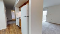 Located at 4101 Pine Oak Circle in Virginia Beach, Virginia, this single-floor residence offers a practical and well-organized layout designed for comfortable everyday living. The kitchen is equipped with full-size white appliances, including a top-freezer refrigerator and an electric range with overhead cabinetry finished in warm wood tones. The kitchen features durable hardwood-style flooring that provides a clean, easy-to-maintain surface. A structural column separates the kitchen from the adjacent living area, creating a natural transition between the two spaces. The living area is finished with plush carpeting, lending a cozy atmosphere underfoot. Natural light is a notable feature of this residence, with a large sliding glass door or window visible from the living space, allowing ample daylight to fill the interior and offering a connection to the outdoors. The overall ambiance is functional and inviting, with a neutral color palette throughout that provides a versatile backdrop for a variety of interior styles. The single-floor layout ensures convenient, step-free access to all areas of the home, making it a practical choice for a wide range of residents.