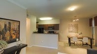 This single-floor residence is designed with an open-concept layout that promotes a seamless flow between the kitchen, dining, and living areas. The kitchen is a standout feature, showcasing dark espresso-toned cabinetry that extends to the upper walls, providing generous storage space. The countertops are finished in granite with rich, multicolored veining, adding a touch of elegance to the functional space. Black appliances, including a refrigerator, microwave, and range, complement the cabinetry for a cohesive, modern aesthetic. A peninsula counter separates the kitchen from the adjoining living and dining spaces, offering both a casual seating option and a natural visual boundary.

The dining area sits just beyond the kitchen, featuring a pendant light fixture with a decorative, multi-bulb design that casts warm light over the dining table. A decorative wall arrangement adds visual interest and personality to the space. Throughout the living and dining areas, light-toned carpet contributes a soft, comfortable feel underfoot. The overall ambiance is warm and welcoming, with recessed and flush-mount lighting ensuring the space is well-illuminated throughout.