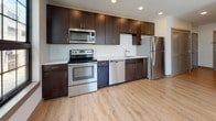 Located at 81 Arch Street in downtown Hartford, Connecticut, this single-floor unit offers a thoughtfully designed layout with modern finishes throughout. The kitchen serves as a standout feature, equipped with a full suite of stainless steel appliances including an electric range, over-the-range microwave, dishwasher, and refrigerator. Rich dark-toned cabinetry extends from floor to ceiling, providing generous storage, while light wood-look flooring and white countertops create a clean, contemporary contrast. A large multi-pane window floods the kitchen with natural light and offers views of the surrounding urban streetscape. The bedroom is a calm, neutral space finished with wall-to-wall carpet and crisp white walls, offering a quiet retreat within the unit. The full bathroom is finished with large-format gray tile flooring, a white soaking tub with shower, a toilet, and a vanity topped with a granite-style countertop and framed mirror. Recessed lighting in the kitchen and consistent, neutral tones throughout the unit contribute to a cohesive, modern aesthetic. The overall design prioritizes functionality and clean lines, making this Hartford address a well-appointed urban residence.