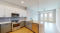 Located at 838 Morrison Dr in Charleston, South Carolina, this single-floor residence showcases a clean, contemporary design throughout. The open-concept kitchen is a standout feature, equipped with stainless steel appliances including a range, microwave, refrigerator, and dishwasher. Two-tone cabinetry pairs white upper cabinets with grey lower cabinets, complemented by a light quartz countertop, a hexagonal tile backsplash, and a peninsula with an undermount sink and matte black faucet. Pendant lighting with glass shades adds a refined touch above the peninsula. Light hardwood-style flooring runs continuously through the kitchen and into the adjoining living area, which benefits from abundant natural light and direct access to a balcony through glass French doors. A ceiling fan in the living area provides comfort year-round. The bathroom is finished with large-format marble-look tile surrounding the tub and shower, a wide vanity with a white countertop, an integrated sink, and matching light wood flooring that ties the space together cohesively. The bedroom offers a spacious, neutral canvas with soft grey walls and the same warm flooring. Built-in shelving near the entry adds practical storage. The overall ambiance is bright, modern, and move-in ready.