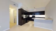 This single-floor residence presents a thoughtfully designed interior that balances style and practicality. The kitchen serves as a central highlight, showcasing rich dark cabinetry that extends from floor to ceiling, creating a bold and sophisticated aesthetic. Granite countertops with subtle speckled patterning provide ample workspace and add a touch of elegance, while a matching kitchen island offers additional prep space and a natural gathering point. Black appliances, including a refrigerator, range, and built-in microwave, complement the dark cabinetry seamlessly. Light-toned tile flooring runs throughout, providing a clean contrast to the darker elements and contributing to an open, airy feel. Recessed and track lighting illuminates the kitchen effectively, enhancing both function and ambiance. A dedicated in-unit laundry area is conveniently located just off the kitchen, housing a full-sized washer and dryer for added everyday convenience. The white walls and ceilings keep the space feeling bright and fresh, while the overall layout flows in a practical and organized manner. This residence combines modern design details with highly functional living spaces.