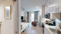 Located on East 6th Street in Austin's dynamic Eastside neighborhood, this efficiently designed one-bedroom, one-bathroom unit offers a thoughtfully arranged open-plan layout on a single floor. The main living area seamlessly integrates the sleeping, living, and kitchen zones into one cohesive space. Light wood-look flooring runs throughout, complemented by soft sage-green accent walls and contemporary framed artwork that add character without overwhelming the interior.

The kitchen is fitted with white cabinetry, stainless steel appliances including a range and microwave, and a compact workspace that maximizes every inch of the footprint. A ceiling fan overhead ensures year-round comfort in the main living area. The sleeping area accommodates a full-size bed flanked by wooden nightstands and table lamps, creating a warm, restful retreat.

The living space features a sofa, round coffee table, and a wall-mounted flat-screen TV paired with a desk and chair. A sliding glass door opens onto a private balcony, bringing in natural light and an outdoor connection. The bathroom is clean and bright, finished in crisp white tones with light wood-look tile flooring, a combination tub and shower, a single vanity, and tasteful decorative accents. The overall ambiance is modern, functional, and move-in ready.