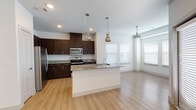 This single-floor residence offers a thoughtfully designed open-concept layout that seamlessly connects the kitchen and living areas, creating a bright and airy atmosphere. The kitchen is a standout feature, anchored by a large center island with a granite countertop and an integrated sink, illuminated by a trio of stylish pendant lights. Rich dark espresso cabinetry lines the walls, complemented by matching granite countertops and a full suite of stainless steel appliances, including a refrigerator, electric range, and over-the-range microwave. Light hardwood flooring flows continuously throughout the space, adding warmth and cohesion. The open living and dining area benefits from abundant natural light streaming through multiple windows fitted with white horizontal blinds. The bedrooms are clean and generously proportioned, each featuring the same hardwood flooring, with at least one offering a walk-in closet. The primary bathroom is well-appointed with a double-sink vanity topped with granite, dark wood cabinetry, a large wall mirror, and a glass-enclosed walk-in shower. A second bathroom features a clean white tiled tub-shower combination with a curved curtain rod. The overall aesthetic is modern and clean, with a neutral color palette.