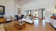 Located at Tanger Outlets Blvd in Pooler, Georgia, this single-floor community clubhouse blends coastal charm with comfortable, functional design throughout its well-appointed spaces. The main gathering area makes an immediate impression with soaring vaulted ceilings clad in white shiplap paneling, rich hardwood flooring, and an abundance of natural light streaming through French doors that open to an outdoor pool area. Coastal-inspired furnishings — including a crisp white sofa, navy wingback chairs, and a distinctive stone-and-glass coffee table — are complemented by nautical artwork and decorative accents that reinforce the relaxed, seaside aesthetic. A dedicated lounge area features soft blue walls, crown molding, ceiling fans, wall-mounted televisions, and a mix of seating arrangements around a trestle dining table, offering a versatile space for both socializing and casual gatherings. The fully equipped kitchen is finished with gray shaker-style cabinetry, light aqua glass tile backsplash, marble-look countertops, and stainless steel appliances, providing ample functionality for community events. A separate recreation room rounds out the space, housing a full-size pool table and additional game and seating areas. Together, these spaces create an inviting, resort-style environment well-suited for community gatherings and leisure activities.