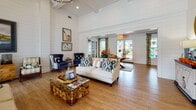 Located at Tanger Outlets Blvd in Pooler, Georgia, this single-floor community clubhouse blends coastal charm with comfortable, functional design throughout its well-appointed spaces. The main gathering area makes an immediate impression with soaring vaulted ceilings clad in white shiplap paneling, rich hardwood flooring, and an abundance of natural light streaming through French doors that open to an outdoor pool area. Coastal-inspired furnishings — including a crisp white sofa, navy wingback chairs, and a distinctive stone-and-glass coffee table — are complemented by nautical artwork and decorative accents that reinforce the relaxed, seaside aesthetic. A dedicated lounge area features soft blue walls, crown molding, ceiling fans, wall-mounted televisions, and a mix of seating arrangements around a trestle dining table, offering a versatile space for both socializing and casual gatherings. The fully equipped kitchen is finished with gray shaker-style cabinetry, light aqua glass tile backsplash, marble-look countertops, and stainless steel appliances, providing ample functionality for community events. A separate recreation room rounds out the space, housing a full-size pool table and additional game and seating areas. Together, these spaces create an inviting, resort-style environment well-suited for community gatherings and leisure activities.