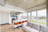 Located on Regent Street in Madison, Wisconsin, this 2-bedroom, 3-bathroom residence delivers a compelling blend of modern design and urban living. The open-concept kitchen and living area serves as the heart of the unit, anchored by a sleek white waterfall island with bar seating, stainless steel appliances, and gray cabinetry. Exposed concrete ceilings with a coffered grid pattern lend an industrial character, while light wood-tone flooring grounds the space with warmth. Floor-to-ceiling windows flood the living area with natural light and frame expansive views of the Madison skyline and surrounding greenery, creating a striking visual backdrop. The primary bedroom is generously proportioned, offering ample space for comfortable living, and is complemented by exposed concrete columns that echo the unit's industrial aesthetic. Each bedroom benefits from natural light and direct access to one of the three well-appointed bathrooms, each featuring clean white quartz countertops, under-mount sinks, large mirrors, and glass-enclosed showers. Light-toned luxury vinyl flooring runs throughout, unifying the space. The overall ambiance is contemporary and functional, with thoughtful architectural details that make this Regent Street residence a standout in Madison's urban landscape.