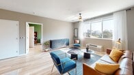 Located on Oneal Street in the heart of Greenville, South Carolina, this thoughtfully designed single-floor residence blends modern aesthetics with functional living. The open-concept layout connects the kitchen, dining, and living areas seamlessly, all finished with warm light wood flooring that flows throughout the space.

The kitchen serves as a central hub, anchored by a striking blue island with a white quartz countertop, pendant lighting, and bar seating. Taupe cabinetry, a stainless steel appliance suite including a French door refrigerator, microwave, and dishwasher, and a classic tile backsplash complete the well-appointed space.

The living area is bright and welcoming, with a large window framing outdoor views of the Greenville skyline and filling the room with natural light. A ceiling fan adds comfort, while neutral walls provide a versatile backdrop.

The bedroom offers a serene retreat, featuring a ceiling fan, a generously sized window with sheer curtains, and access to closet storage. The bathroom is clean and contemporary, with large-format tile flooring, a dark vanity with white countertop, an illuminated mirror, and a tiled shower. The entry foyer provides a smooth transition into the home, with clean lines and ample circulation space.