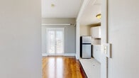 Located in the heart of San Diego's Bankers Hill neighborhood, this thoughtfully designed one-bedroom unit offers a compelling blend of classic architectural details and comfortable living. The main living area showcases gleaming hardwood floors, neutral gray-toned walls, and a pair of striking arched windows that flood the space with natural light and frame sweeping views of the surrounding cityscape. A ceiling fan adds practical comfort overhead, while elegant French doors open directly onto a private deck — a standout feature of the unit. The covered outdoor deck is anchored by a pergola supported by stately columns and finished with decorative iron railings, creating an ideal space for outdoor relaxation with open views of the San Diego skyline. The generously proportioned bedroom features plush carpet flooring, soft neutral walls, and access to a vanity area with a classic oval mirror and dark cabinetry. The kitchen is well-appointed with white cabinetry, tile countertops, classic penny-tile flooring, and stainless steel appliances including a gas range and full-size refrigerator, complemented by a window for natural ventilation. A separate, carpeted room provides additional flexible living space. Throughout, crisp white trim and consistent neutral tones create a cohesive, inviting atmosphere.