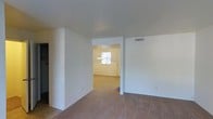 Located at 101 Tanglewood Dr in Southern Pines, NC, this single-story home offers a straightforward and functional layout designed for comfortable everyday living. The interior features a neutral color palette with crisp white walls that create a bright, clean atmosphere throughout. Carpeted flooring runs through the main living areas, adding warmth and a sense of coziness underfoot, while tiled flooring is present in transitional spaces. The open flow between rooms allows natural light to travel freely from one area to the next, with a window near the entryway drawing in daylight and illuminating the connected spaces. A pendant light fixture is visible in the dining or entry area, providing a focal point and supplemental lighting. Ceiling-mounted HVAC vents are integrated throughout, ensuring consistent climate control. The home's layout connects the living area to adjacent rooms with open passageways, creating an easy, unobstructed flow. The overall ambiance is calm and neutral, offering a move-in ready canvas that is well-suited for a variety of interior styles and furnishing preferences.